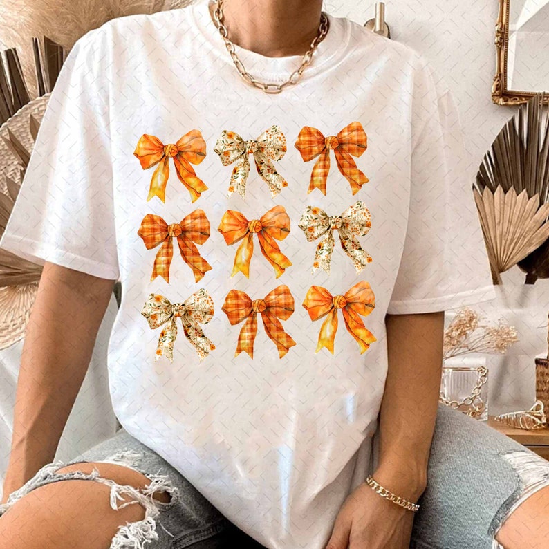 May include: White t-shirt with a pattern of nine orange and white bows. The bows are arranged in three rows of three.