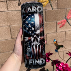 May include: A black and red stainless steel tumbler with a skull graphic and an American flag design. The text "KARO FIND" is printed on the tumbler.