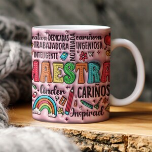 May include: A pink ceramic mug with a colorful design that says "Maestra" and includes words like "creativa", "dedicada", "cari&ntilde;osa", "motivada", "trabajadora", "ingeniosa", "inteligente", "linda", "cari&ntilde;os", and "inspirad".