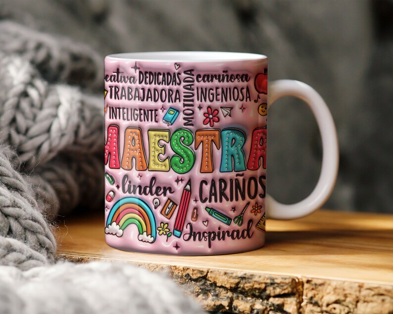 May include: A pink ceramic mug with a colorful design that says "Maestra" and includes words like "creativa", "dedicada", "cari&ntilde;osa", "motivada", "trabajadora", "ingeniosa", "inteligente", "linda", "cari&ntilde;os", and "inspirad".