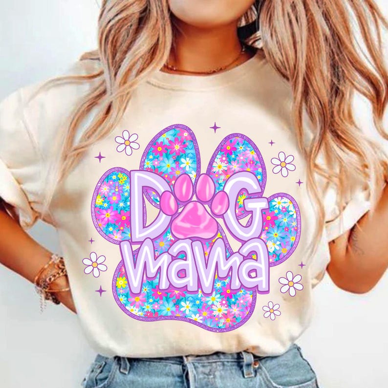 May include: White t-shirt with a purple paw print design. The paw print is filled with colorful flowers and the text "Dog Mama" is written in purple letters.