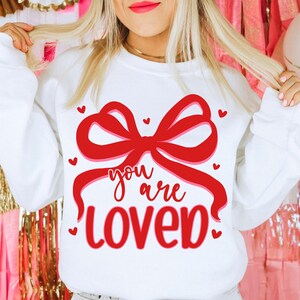 May include: White sweatshirt with a red bow and the text "you are loved" in red.