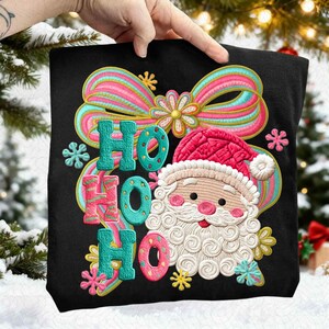 Peut inclure: Sac fourre-tout noir avec un motif brodé du Père Noël et les mots "HO HO HO". Le motif comprend un nœud rose et bleu, des flocons de neige et un bonnet de Père Noël.