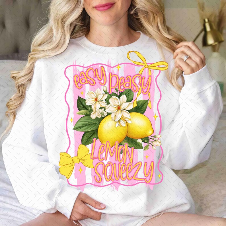 Op de afbeelding: Witte trui met een roze en witte gestreepte achtergrond. De tekst "easy peasy lemon squeezy" is in roze en geel geschreven. Er zijn gele citroenen en witte bloemen op het ontwerp.