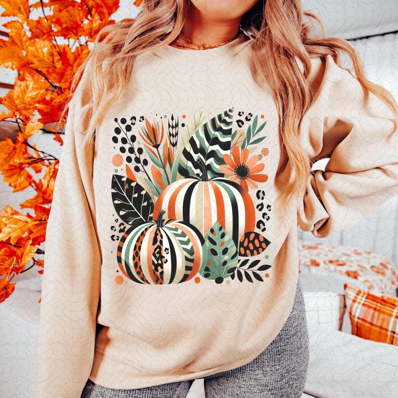 Peut inclure: Un sweat-shirt beige avec un imprim&eacute; graphique de citrouilles, de feuilles et de fleurs dans des tons d'orange, de vert et de marron. Le design a un aspect vintage et automnal.