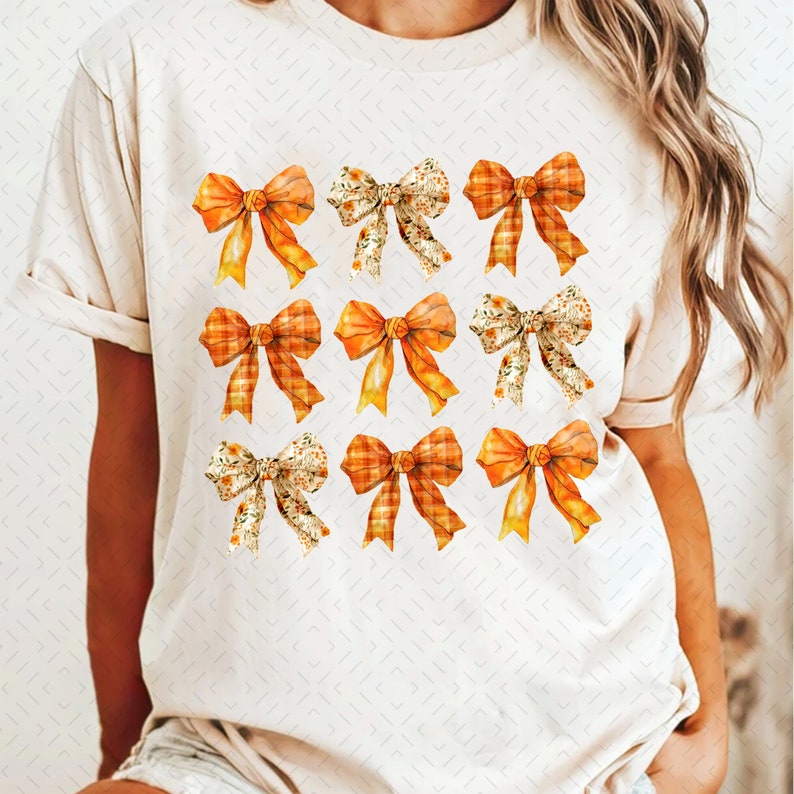 May include: A white t-shirt with a pattern of nine orange and yellow bows. The bows are in a variety of styles, including plaid, floral, and solid.