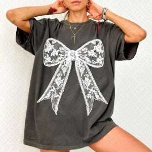 May include: A dark gray oversized t-shirt with a white lace bow graphic.