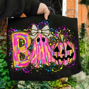 May include: Black tote bag featuring a colorful Halloween design. The design includes a pink and yellow letter "B", a ghost with a bow, and a jack-o'-lantern. The word "Boo" is implied. The design is accented with colorful paint splatters.