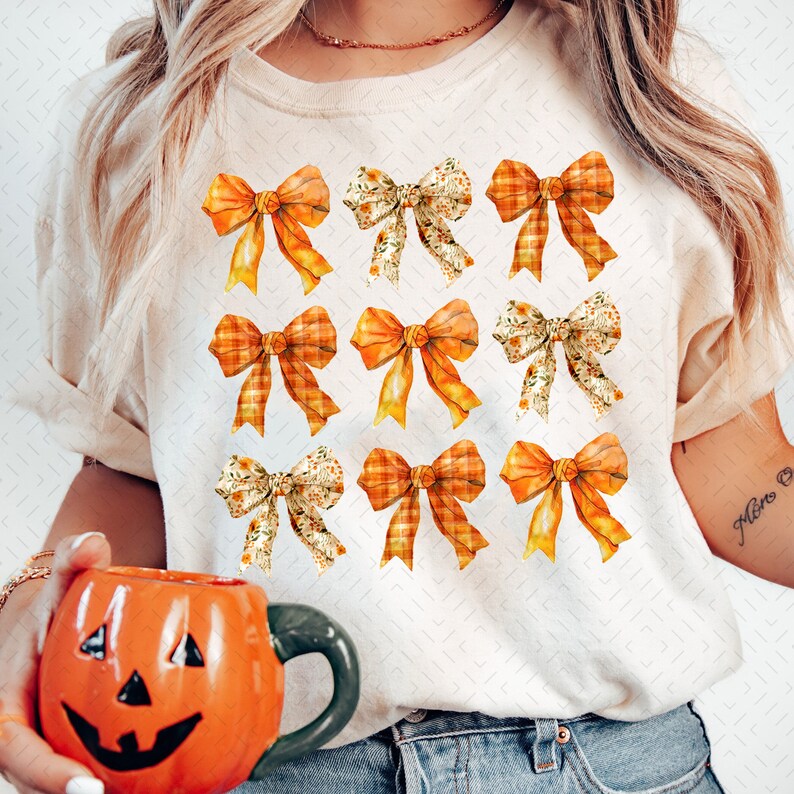 May include: A white t-shirt with a pattern of nine orange and yellow bows. The bows are arranged in a grid pattern and have different designs, including plaid and floral.