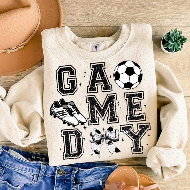 May include: A beige sweatshirt with the text "GAME DAY" in black with a soccer ball, soccer cleats, and a bow.