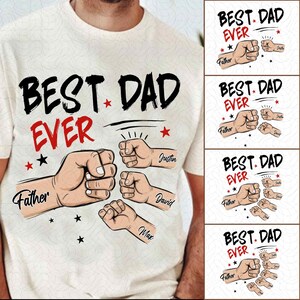 Pode incluir: Camiseta creme com o texto "BEST DAD EVER" em preto e vermelho, apresentando ilustrações de punhos e os nomes "Father", "Justin", "David" e "Max". O design inclui estrelas.
