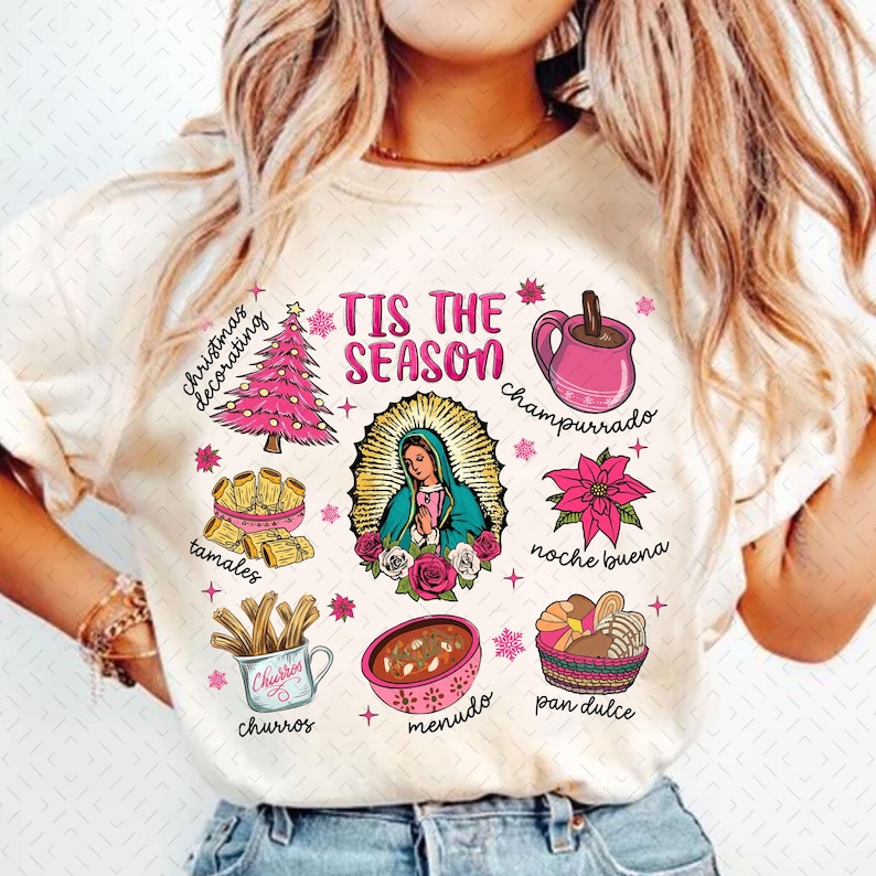 May include: A white t-shirt with a pink and white design featuring the text "Tis the Season" and various Mexican Christmas traditions, including tamales, churros, champurrado, and pan dulce.