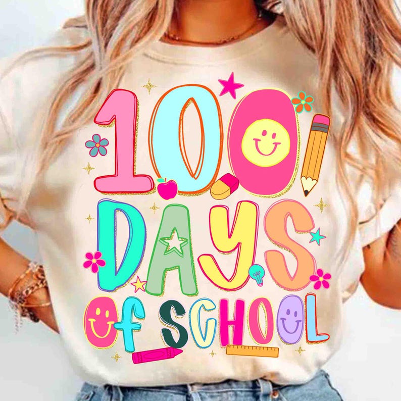 May include: A cream-coloured t-shirt featuring a vibrant graphic celebrating "100 Days of School." The design includes the numbers "100" in pink and blue, the words "Days of School" in bright colours, and playful illustrations.