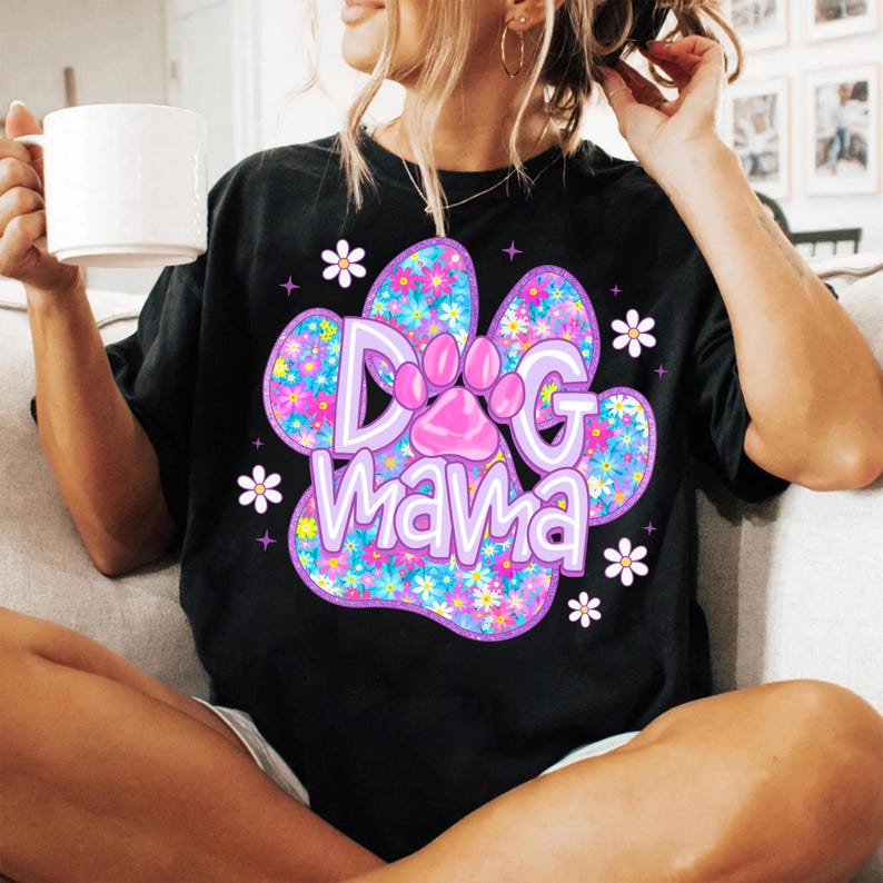 May include: Black t-shirt with a purple paw print design. The paw print is filled with colorful flowers and the text "Dog mama" is written inside the paw print.