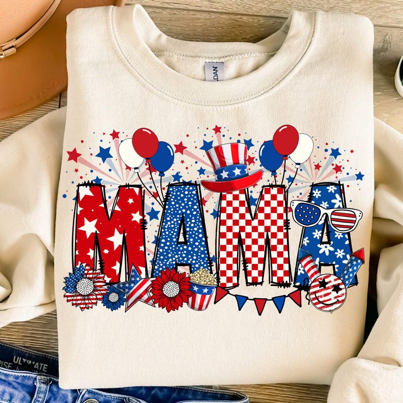 May include: A cream-colored sweatshirt with a red, white, and blue graphic design that says "MAMA" with stars, fireworks, and other patriotic imagery.