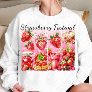 Op de afbeelding: Wit sweatshirt met een roze en rood aardbeienfestival ontwerp. Het ontwerp bevat aardbeien, een pot jam, een aardbeientaart, een glas aardbeisap en een strohoed.