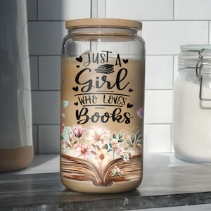 K&ouml;nnte beinhalten: Ein Glasgef&auml;&szlig; mit einem Holzdeckel und einem Blumendesign. Das Gef&auml;&szlig; tr&auml;gt ein Zitat, das lautet "Just a girl who loves books" mit einem Stapel B&uuml;cher und Herzen.