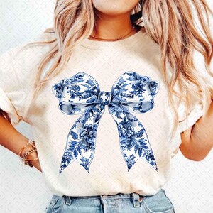 May include: A white t-shirt with a blue and white floral bow design.