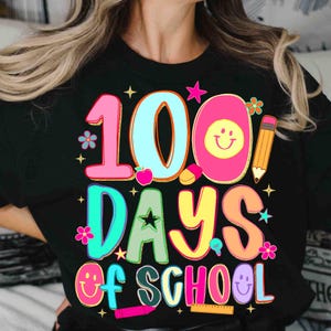 May include: Black t-shirt with a vibrant graphic celebrating 100 days of school. The design includes the number "100" in pink and blue, the words "DAYS OF SCHOOL" in various colours, and school-themed illustrations.