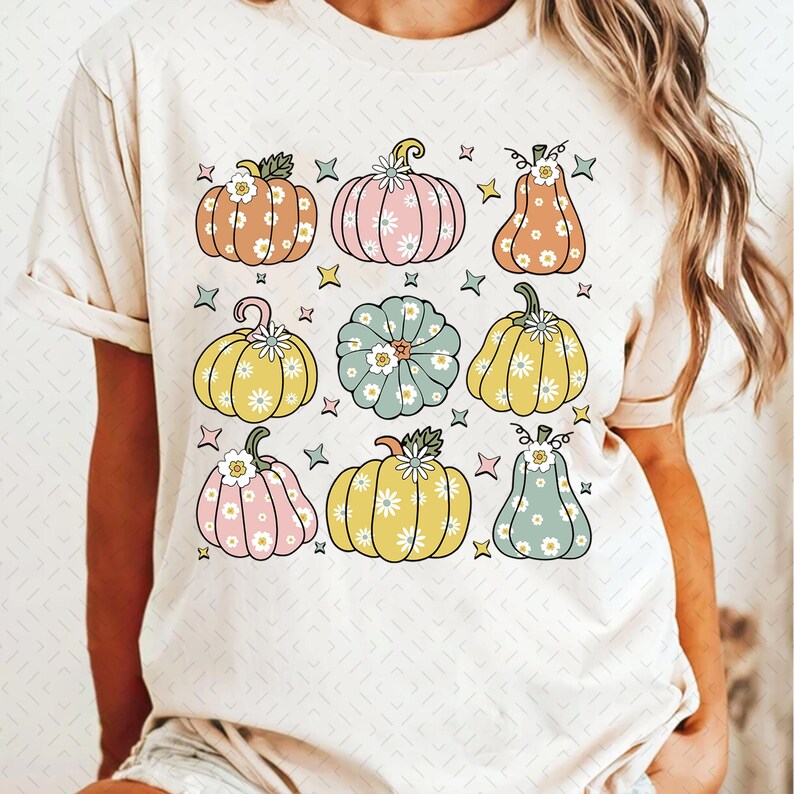 May include: A white t-shirt with a pattern of colorful pumpkins with floral designs. The pumpkins are in various shades of pink, yellow, green, and orange.
