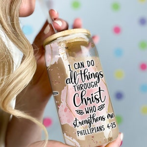 May include: A clear glass tumbler with a wooden lid and a straw. The tumbler has a pink and gold watercolor design with the text "I can do all things through Christ who strengthens me Philippians 4:13".