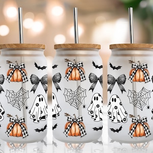 May include: Three white tumblers with wooden lids and stainless steel straws. Each tumbler features a Halloween-themed design with black bats, spiderwebs, ghosts, and pumpkins with black and white checkered bows.