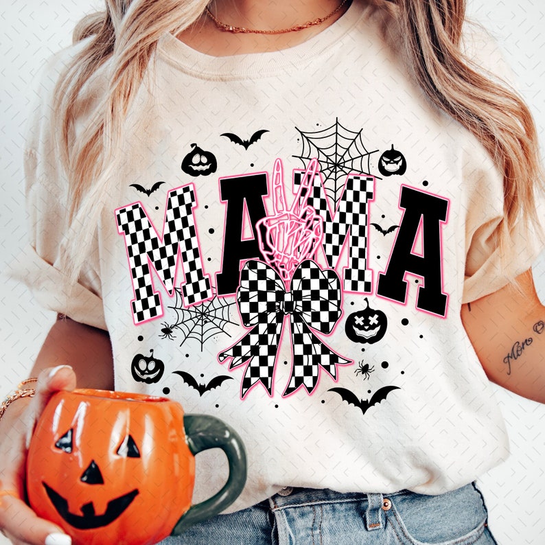 May include: A white t-shirt with a black and white checkered "MAMA" graphic. The graphic includes a pink bow with a skeleton hand peace sign in the center. The shirt is decorated with bats, spiders, and pumpkins.