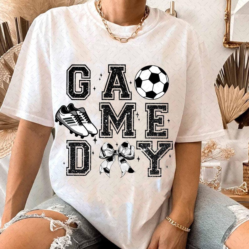 May include: White t-shirt with black glitter text that reads "GAME DAY" with a soccer ball, soccer cleats, and a bow.