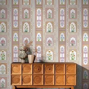 May include: A wooden dresser with a mid-century modern design. The dresser has a light brown finish and features a repeating pattern of circular cutouts on the front. The dresser is in front of a wall with a patterned wallpaper featuring a repeating design of floral motifs and arches in shades of pink, beige, and blue.
