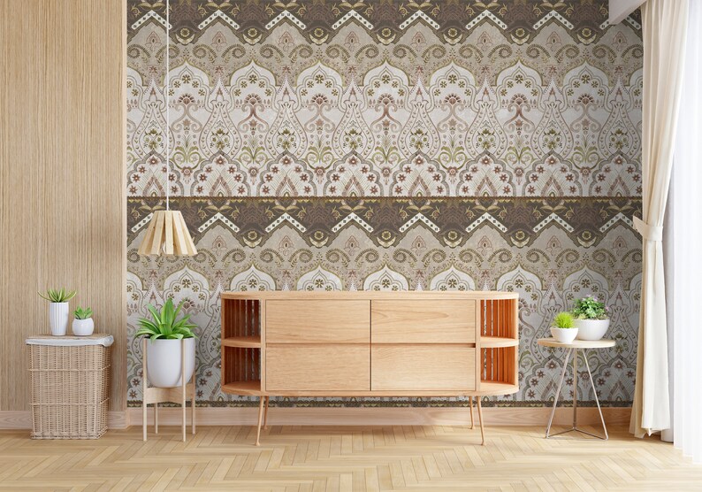 May include: A wooden dresser with four drawers sits in front of a wall with a patterned wallpaper. The wallpaper features a repeating design of brown, beige, and gold arches with intricate details. The dresser has a light wood finish and is accented with a decorative trim.