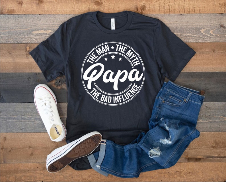 May include: A black t-shirt with a white circle graphic that says "The Man * The Myth * Papa * The Bad Influence".