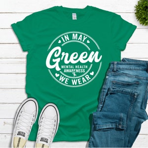 May include: Green t-shirt with a white circle graphic that says "In May We Wear Green" and "Mental Health Awareness".