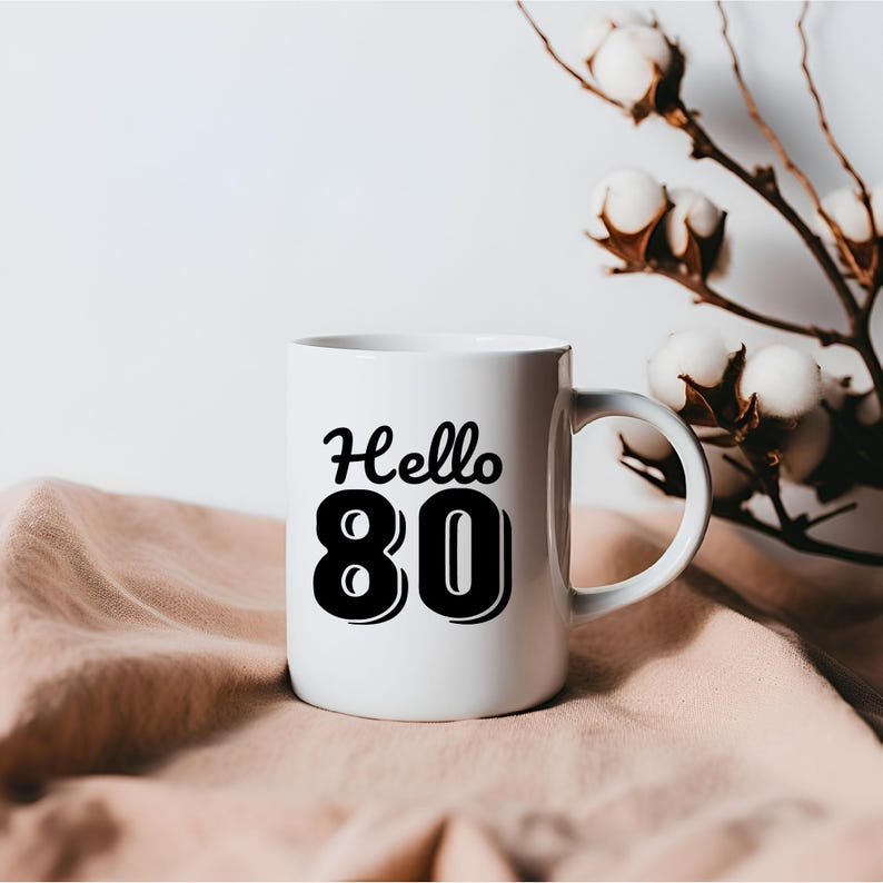 May include: White ceramic mug with a black design that says "Hello 80" in a retro font.