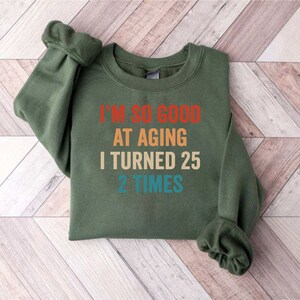 May include: A green sweatshirt with the text "I'm so good at aging I turned 25 2 times" in a rainbow color scheme.