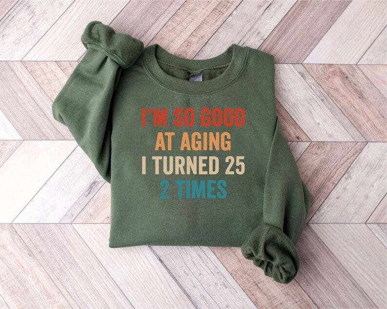 May include: A green sweatshirt with the text "I'm so good at aging I turned 25 2 times" in a rainbow color scheme.