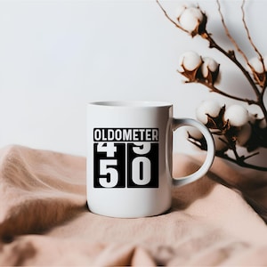 May include: White ceramic mug with a black design that says "Oldometer 49 50".