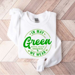 May include: White sweatshirt with a green circle graphic that says "In May We Wear Green" with the text "Mental Health Awareness" inside the circle.