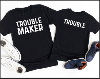 May include: Matching black t-shirts with white text. One shirt says "Trouble Maker" and the other says "Trouble".