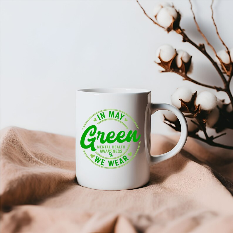 May include: White ceramic mug with a green circle design that says "In May We Wear Green" with a green ribbon symbol and the words "Mental Health Awareness".