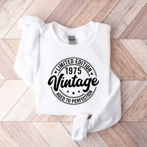 May include: White sweatshirt with a black circle graphic that says "Limited Edition 1975 Vintage Aged to Perfection".