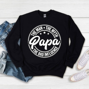 May include: Black sweatshirt with a white circle graphic that says "The Man * The Myth * Papa * The Bad Influence".