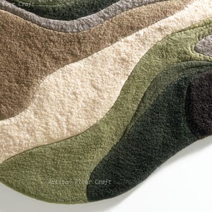 May include: A soft, abstract rug with a unique, organic shape. The rug features a layered design with wavy bands of color, including shades of brown, beige, green, and black. The texture appears plush and inviting, suitable for a living space.