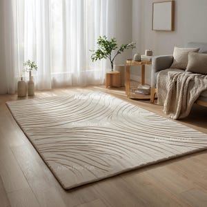Puede incluir: Alfombra rectangular beige con un diseño tallado y fluido. La alfombra está colocada sobre un suelo de madera en un salón. El diseño presenta líneas curvas, creando una apariencia texturizada. Las palabras "Artisan Floor Craft" están impresas en la alfombra. Mide aprox. 240 cm x 300 cm.
