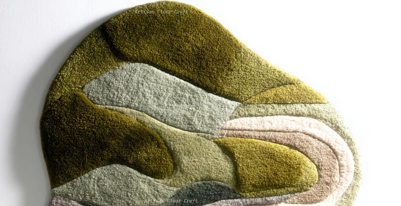 May include: A textured, abstract rug with a layered design in shades of green, gray, and beige. The rug features a soft, plush texture and a unique, organic shape. The words "Artisan Floor Craft" are printed on the rug.