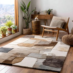 May include: A rectangular rug featuring an abstract stone design in shades of brown, beige, grey, and white. The rug is placed on a wooden floor in a room with natural light and a view of a city. The rug's design adds a modern touch to the room.