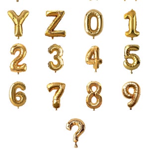 Puede incluir: Globos de letras y n&uacute;meros de l&aacute;mina dorada, incluyendo las letras de la U a la Z, los n&uacute;meros del 0 al 9 y un signo de interrogaci&oacute;n. Los globos est&aacute;n inflados y aislados sobre un fondo blanco.