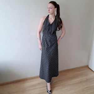 Pode incluir: Um conjunto de top e saia pretos e brancos. O top tem riscas verticais e botões na frente. A saia é longa, com um padrão xadrez. A roupa é combinada com saltos pretos e brancos.