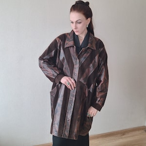 Può includere: Un cappotto in pelle marrone con un motivo geometrico unico. Il cappotto presenta una chiusura con bottoni, maniche lunghe e un colletto. Il design incorpora varie tonalità di marrone, creando un aspetto visivamente sorprendente e strutturato.