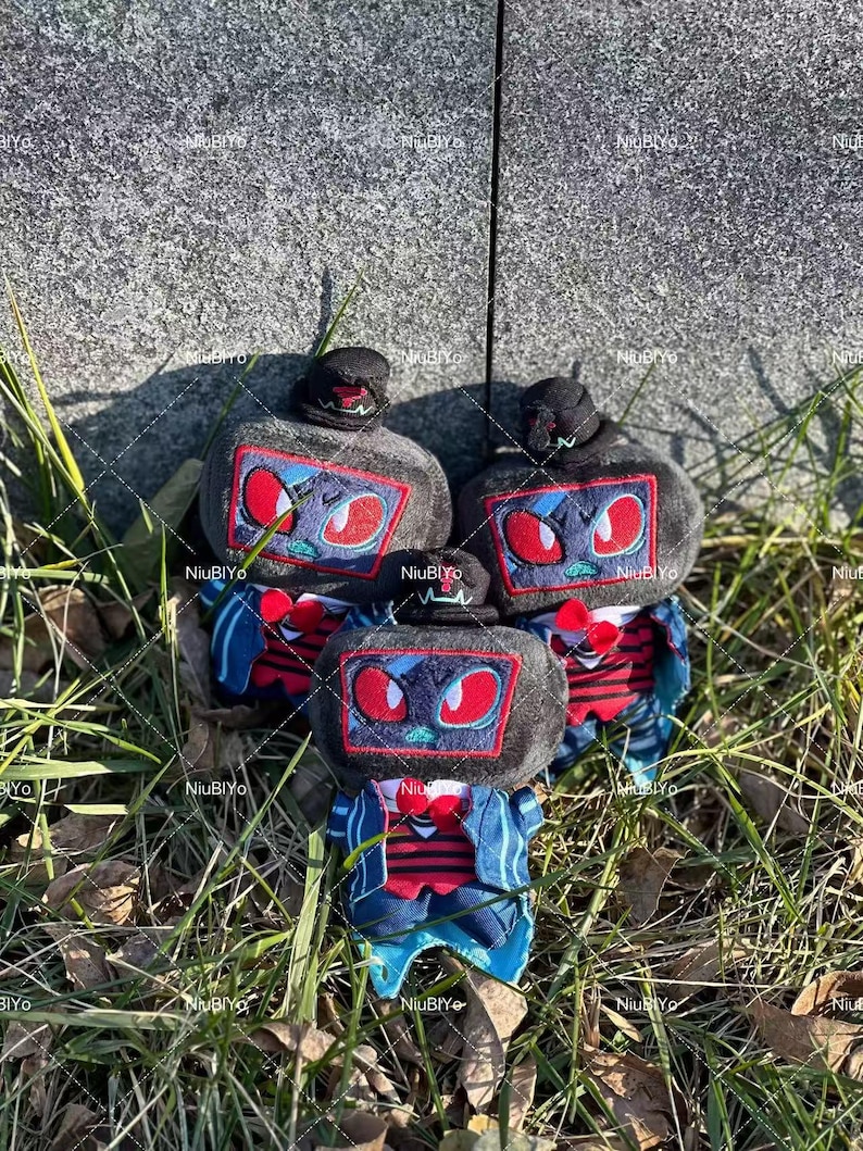 May include: Three plush toys with a robot design. Each has a black hat, a grey body with a screen-like face featuring red eyes, and a red bow tie. The toys are wearing blue jackets with red and white striped shirts.