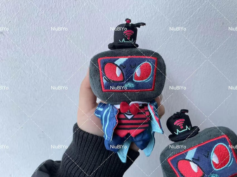 May include: A plush toy in the shape of a retro television set, complete with a top hat. The toy is grey with a screen showing red eyes and a blue design. It wears a red bow tie and a blue and red outfit. Another toy is also visible.